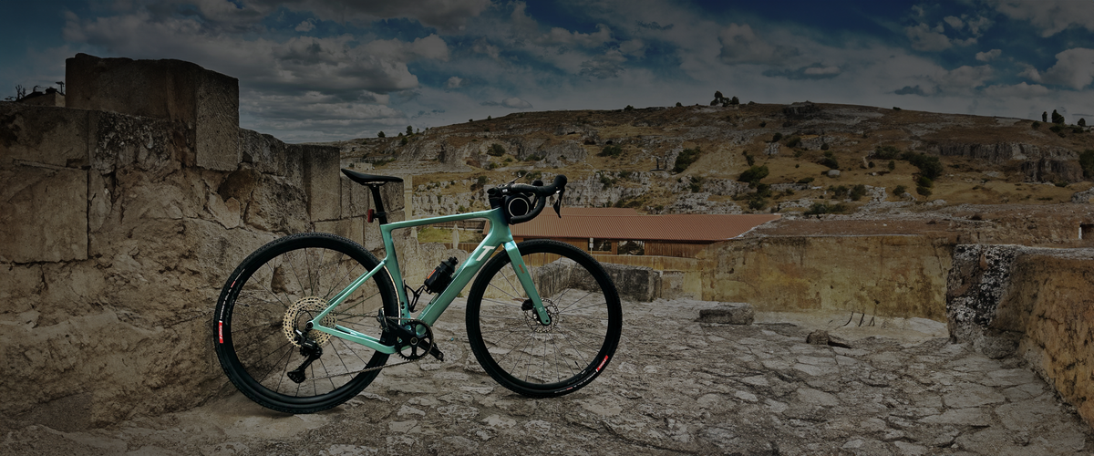 Bici gravel 3T Racemax WPNT appoggiata a un muro in pietra, con colline rocciose sullo sfondo